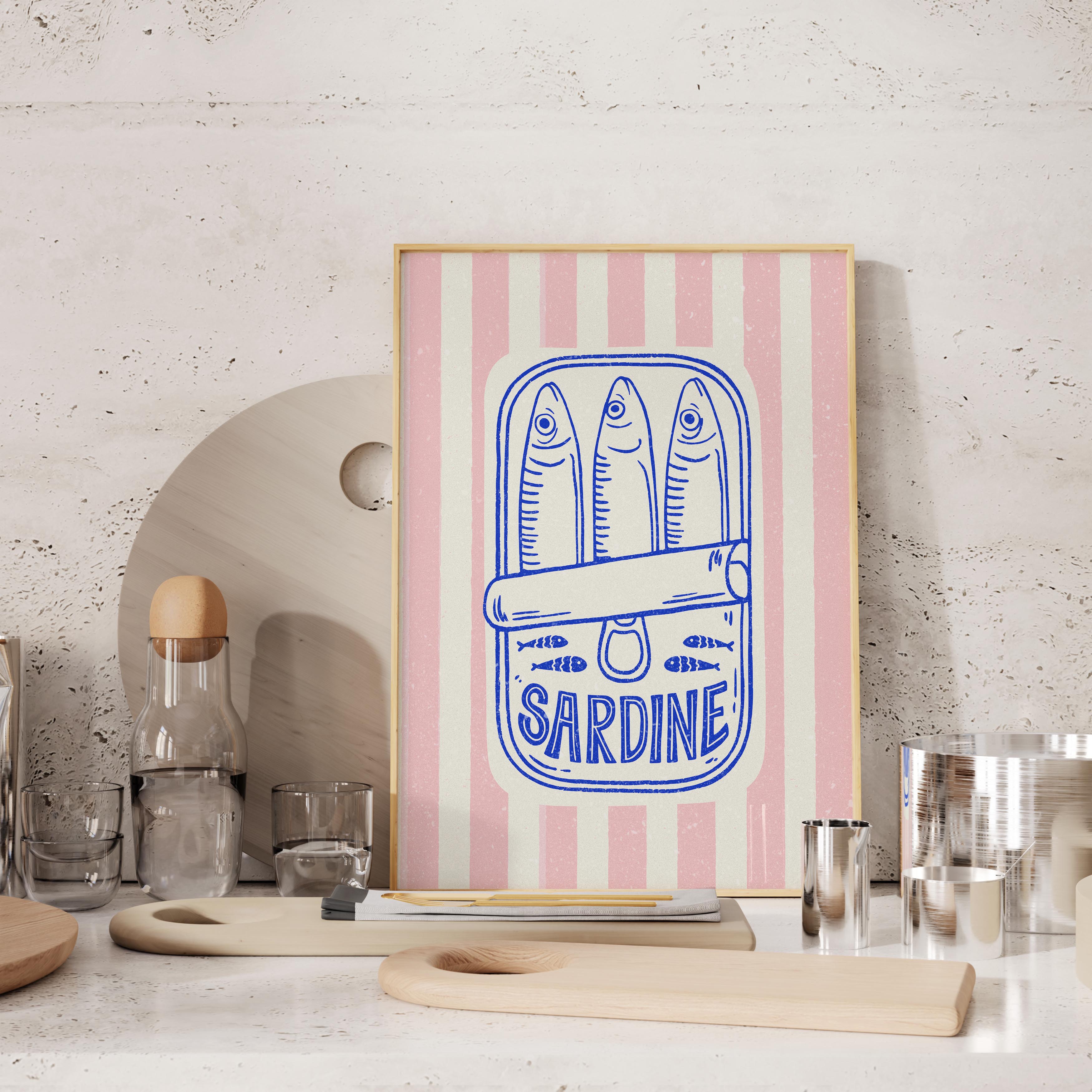 a framed artwork with a pink and white striped background, depicting a can of Sardine with three fish. The artwork is placed on a table with various kitchen items, such as a bottle, a glass, and a wooden cutting board.
