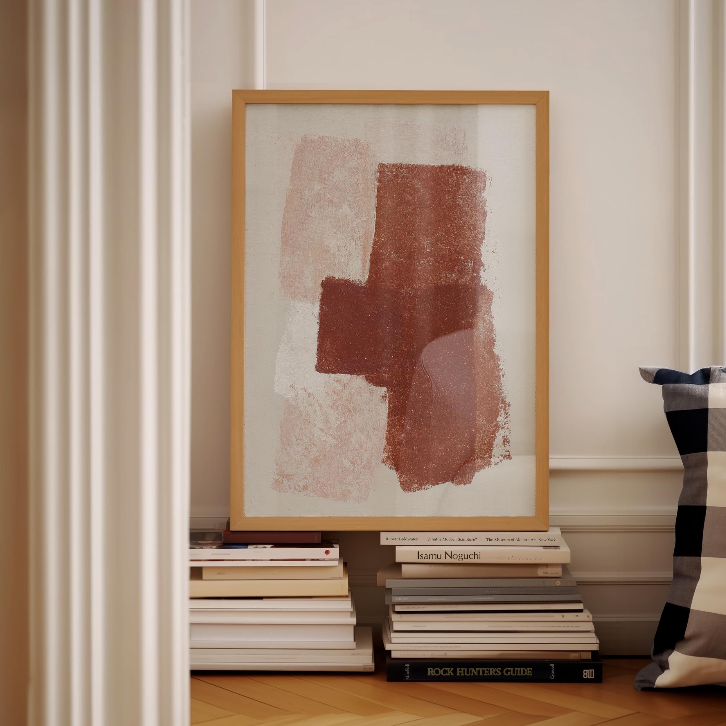 a framed abstract painting on a white wall, with a stack of books and a pillow visible below it.