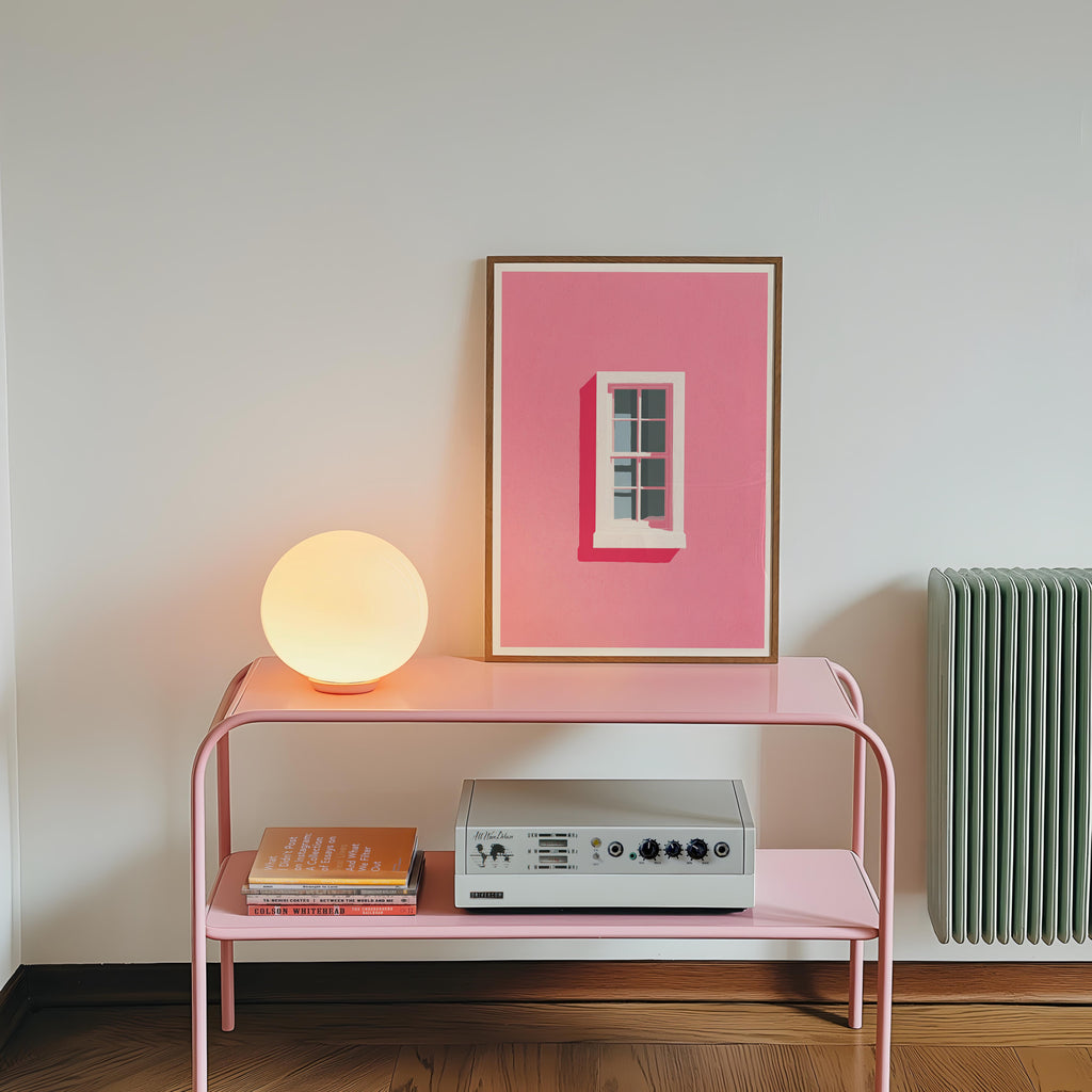 a pink table with a lamp, a framed artwork of a pink window, and a white stereo system on it.