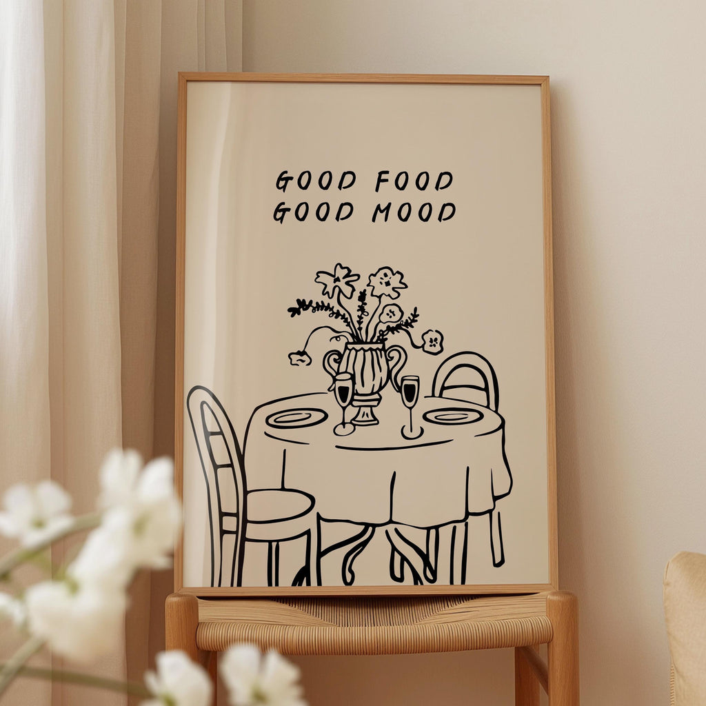 a framed illustration of a table with a vase of flowers, accompanied by the text "GOOD FOOD GOOD MOOD" above it.