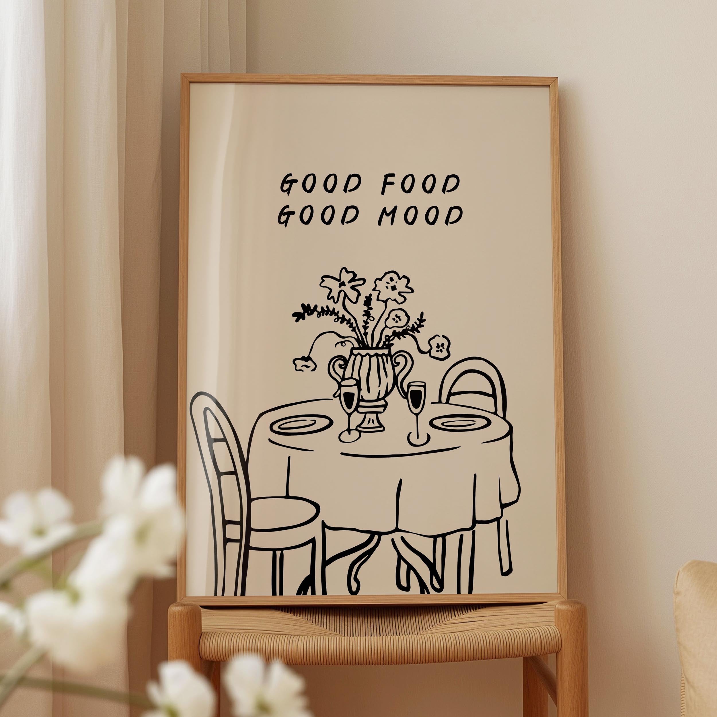 a framed illustration of a table with a vase of flowers, accompanied by the text "GOOD FOOD GOOD MOOD" above it.