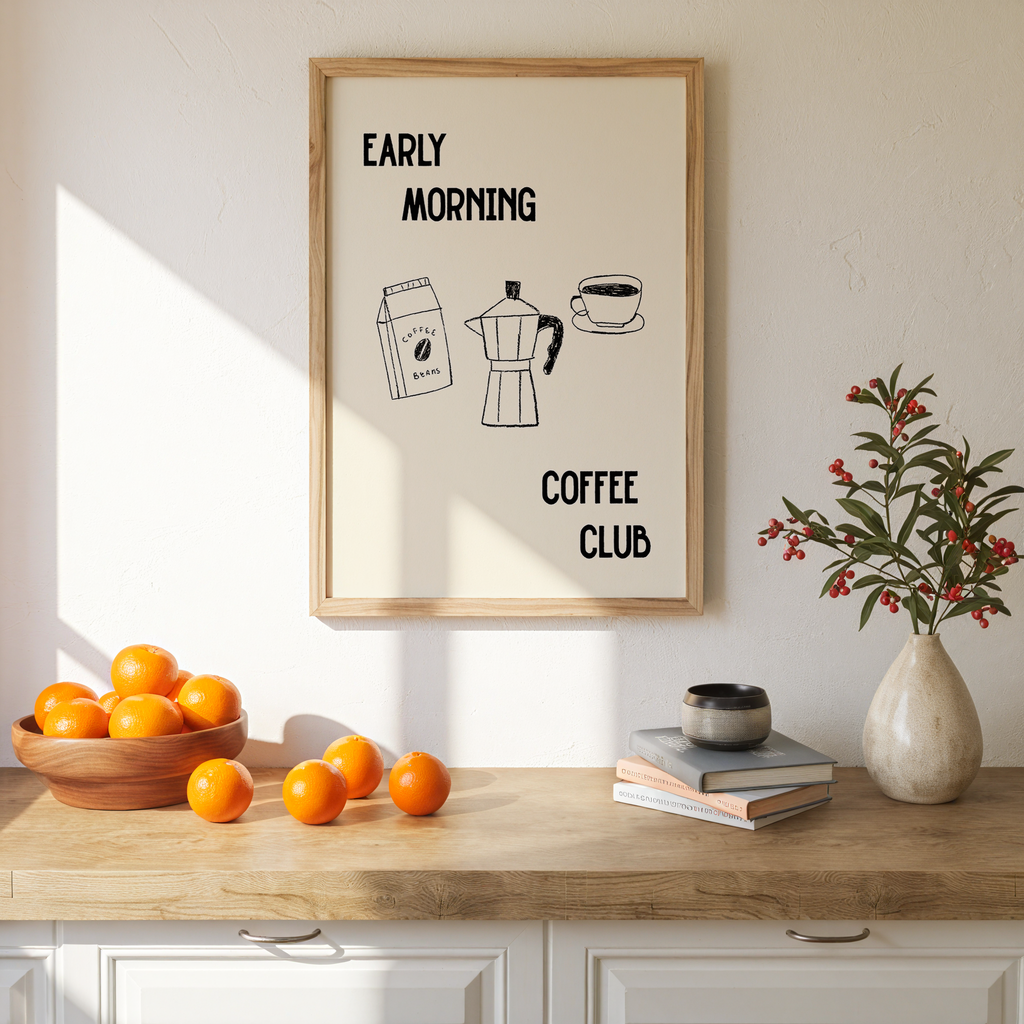 a kitchen counter with a framed poster that reads "Early Morning Coffee Club" above a bowl of oranges and a vase of flowers.