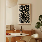 a dining area with a table set for two, a bottle of wine, and a framed abstract leaf-like artwork on the wall.