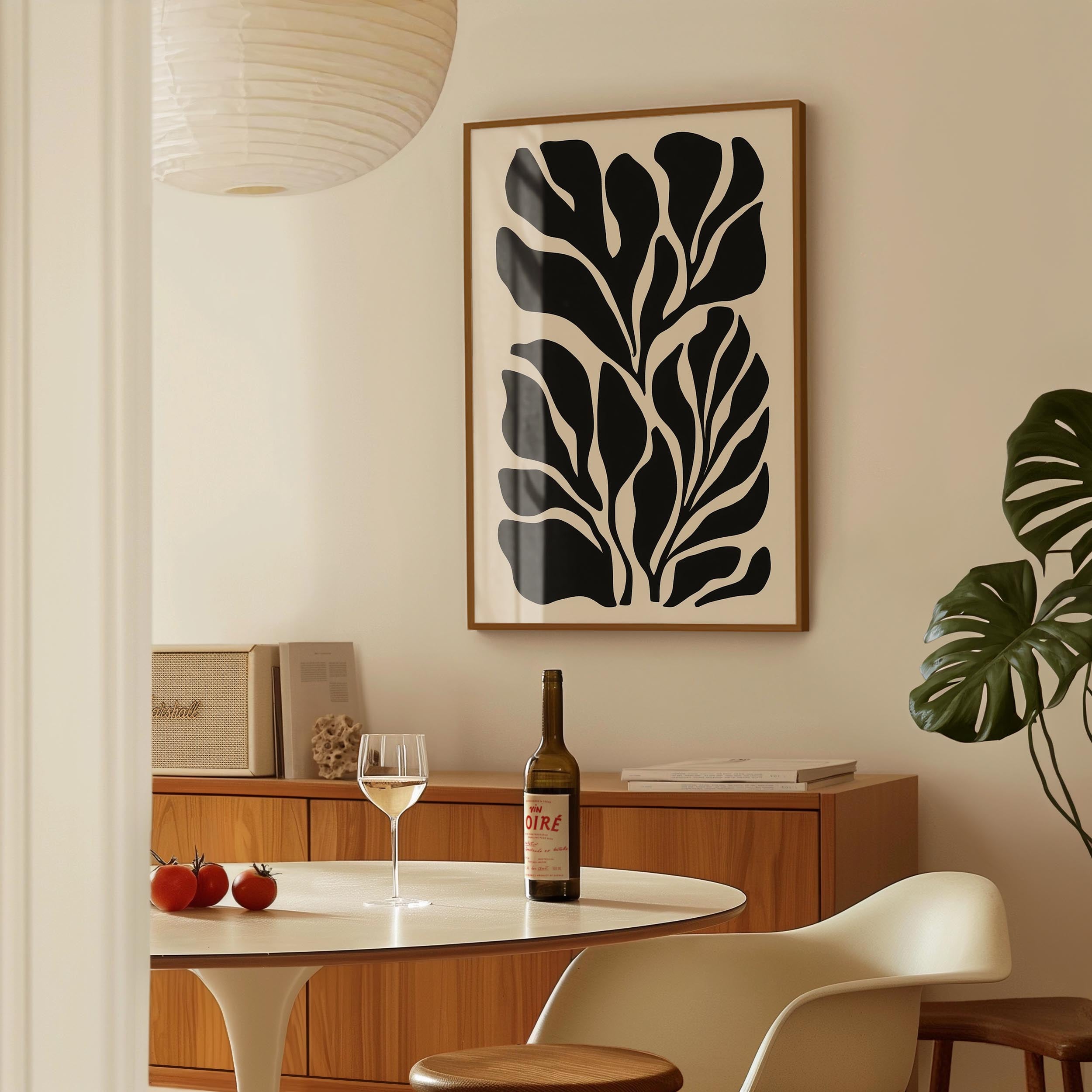 a dining area with a table set for two, a bottle of wine, and a framed abstract leaf-like artwork on the wall.