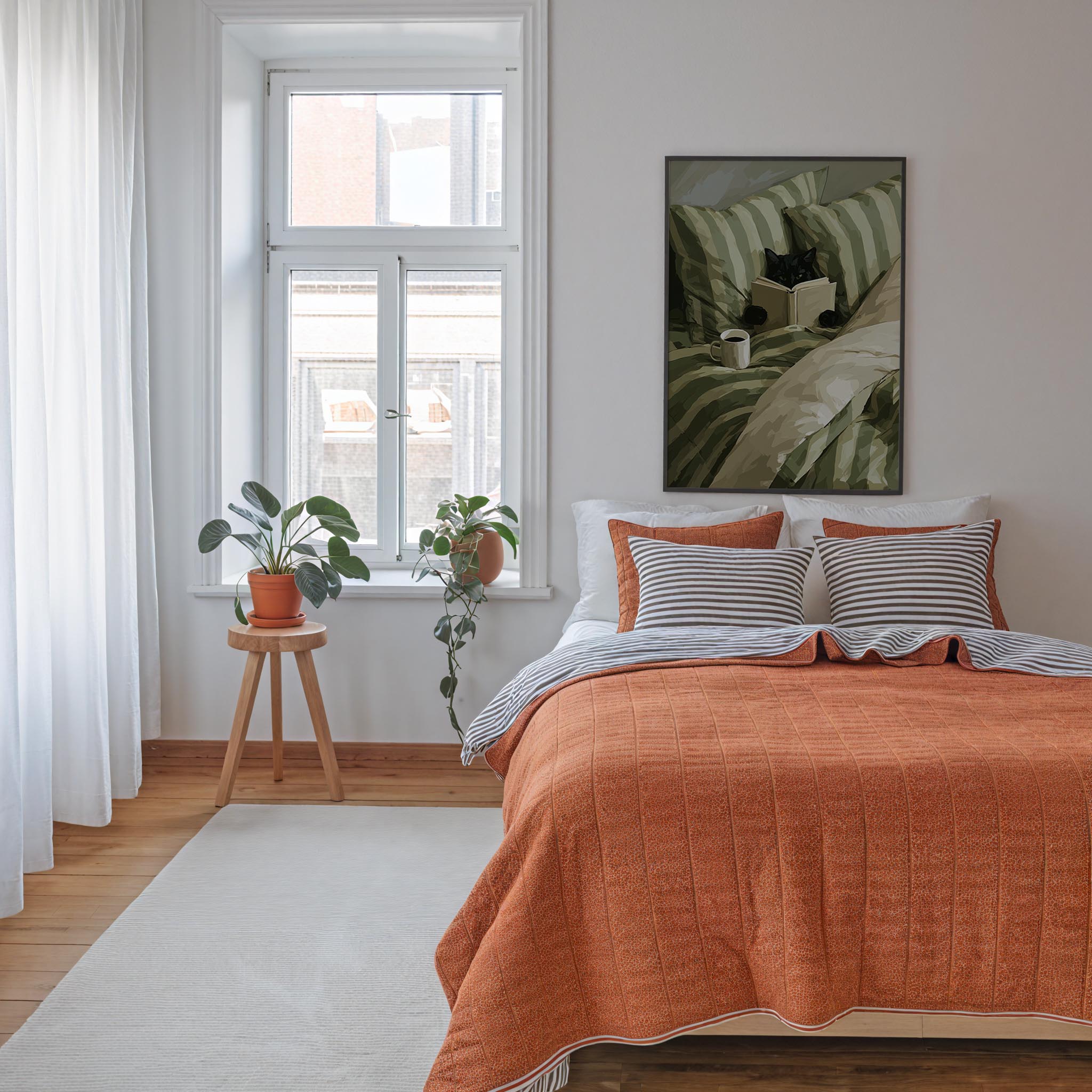 a cozy bedroom with a large bed, a wooden stool with a potted plant, and a framed artwork on the wall.