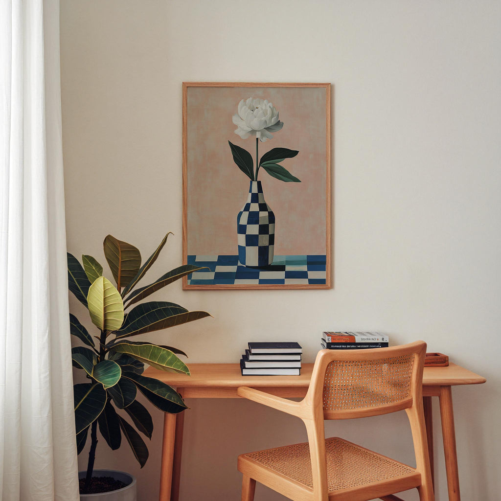 a wooden desk with a stack of books on it, a potted plant, and a framed painting of a flower on the wall above the desk.