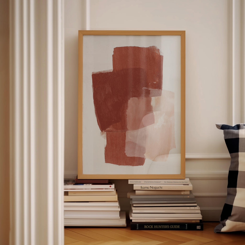 a framed abstract painting on a white wall, with a stack of books and a pillow visible below it.