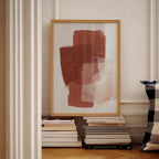 a framed abstract painting on a white wall, with a stack of books and a pillow visible below it.