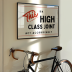 a framed sign with the text "This is a HIGH CLASS JOINT ACT ACCORDINGLY" hanging on a wall above a bicycle.