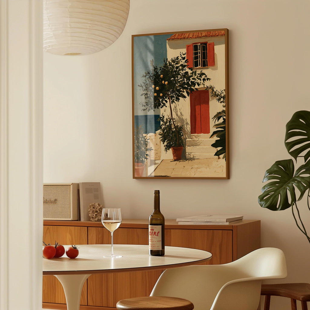 a dining area with a table set for two, a bottle of wine, and a framed painting of a house with a tree and a door.
