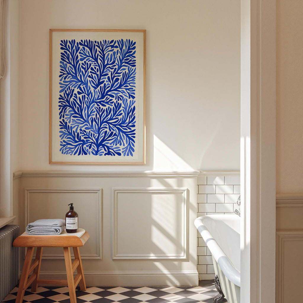 a bathroom with a white bathtub, a framed blue floral print on the wall, and a wooden stool with a bottle of soap on it.