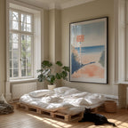 A cozy bedroom with a large window, a bed with white sheets, a potted plant, and a framed artwork depicting a beach scene. A black cat is sitting on the floor in front of the bed.