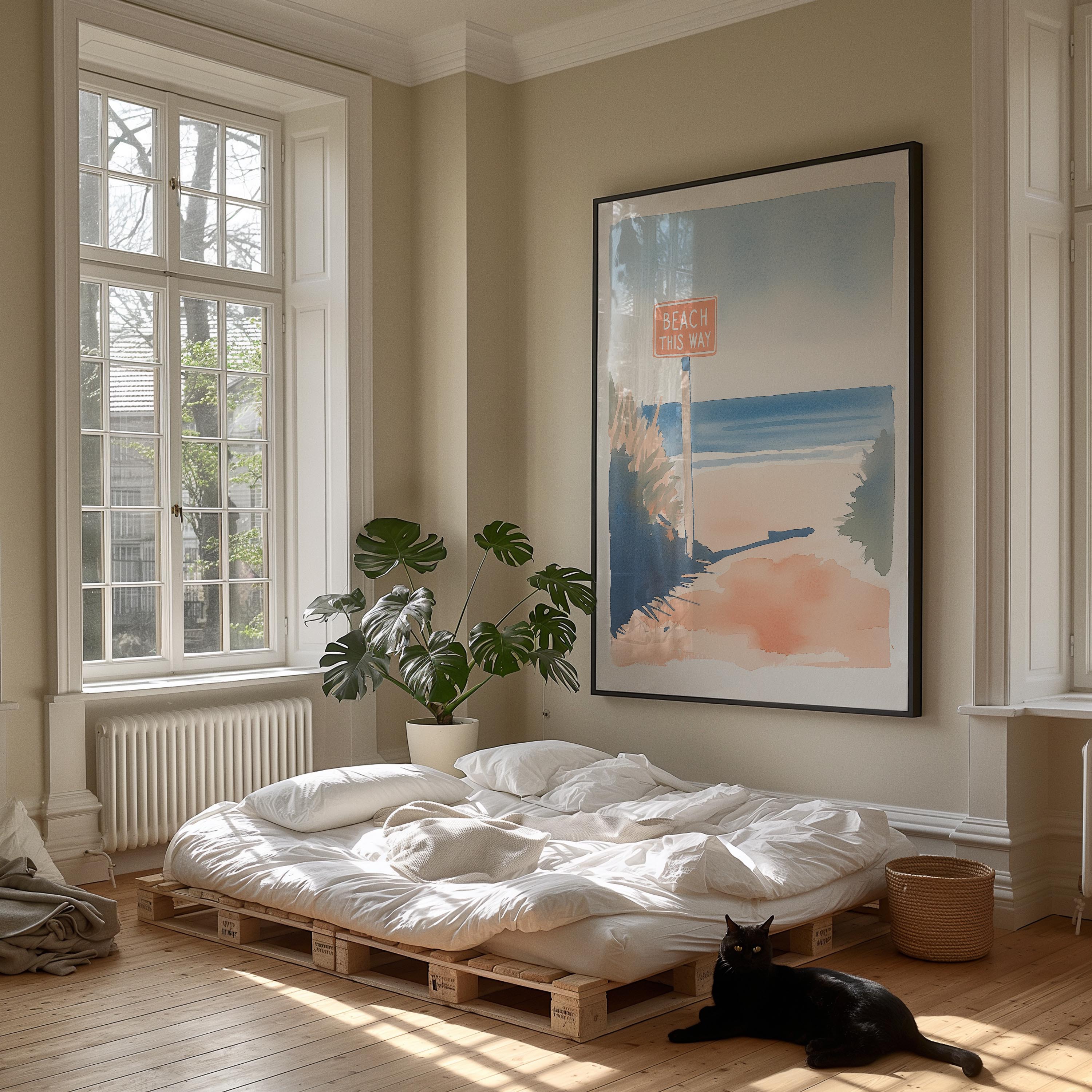 A cozy bedroom with a large window, a bed with white sheets, a potted plant, and a framed artwork depicting a beach scene. A black cat is sitting on the floor in front of the bed.