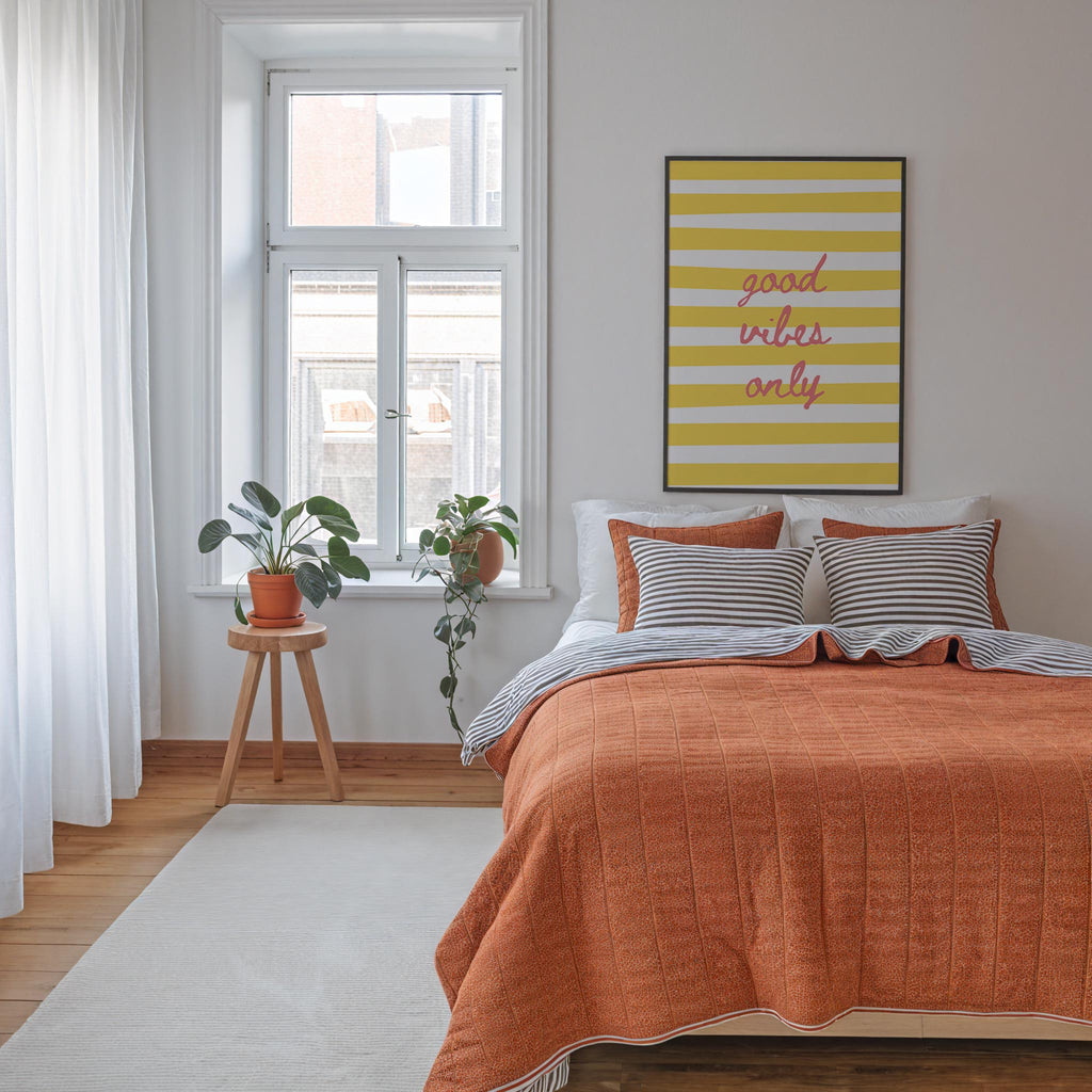 a cozy bedroom with a large bed, a wooden stool with a potted plant, and a yellow and white striped poster on the wall.