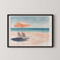 A framed watercolor painting depicting a serene beach scene with two lounge chairs under an orange umbrella, overlooking the ocean.