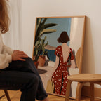A person is sitting in front of a large painting depicting a woman in a red dress with white polka dots, looking out a window.