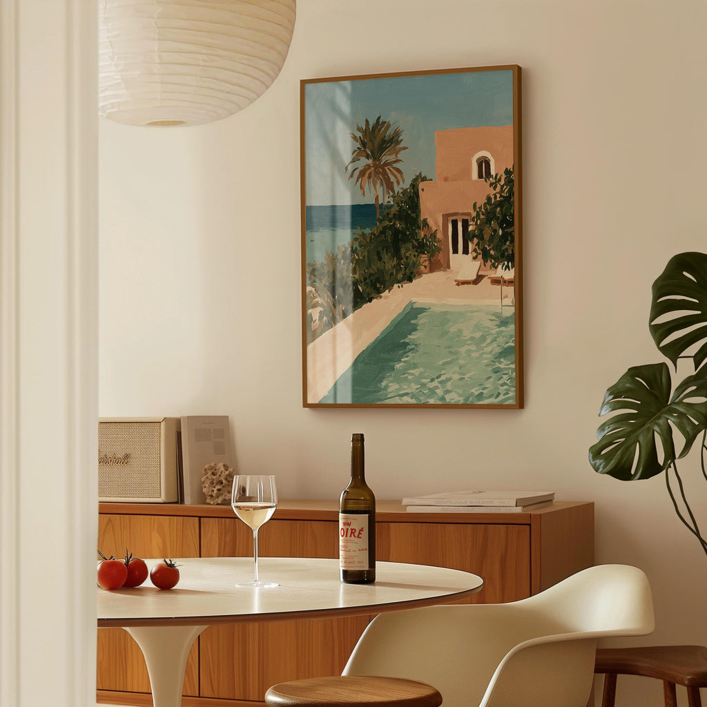 a dining area with a table set for two, a bottle of wine, and a framed painting of a tropical beach scene hanging on the wall.