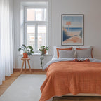 a cozy bedroom with a large bed, a wooden stool with a potted plant, and a framed artwork of a beach scene on the wall.