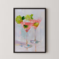 The image is a framed painting depicting two martini glasses filled with a pink drink, garnished with lime slices and a sprig of mint.