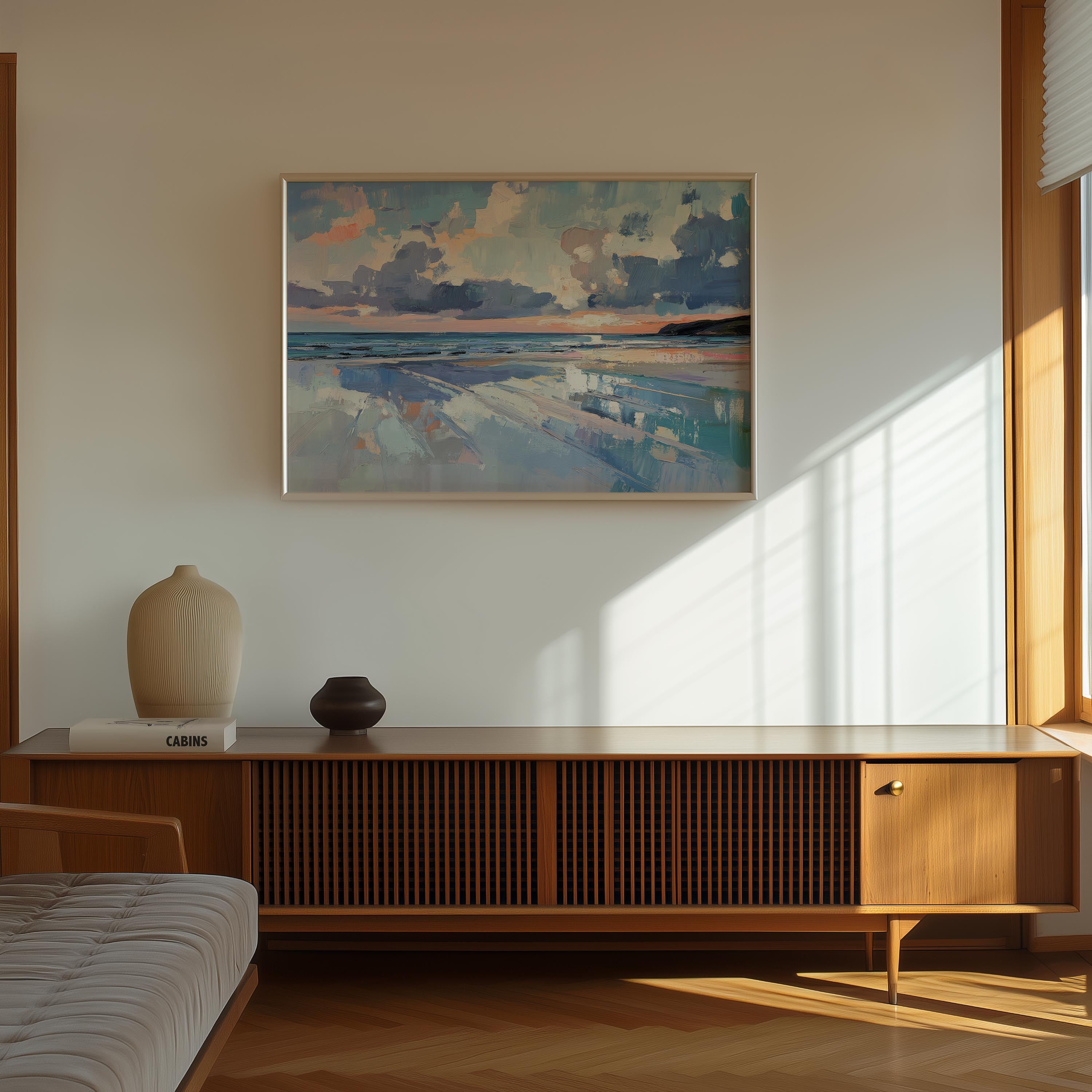 a serene indoor setting with a large painting of a beach scene hanging on the wall above a wooden cabinet or entertainment center. The painting depicts a tranquil beach landscape with a cloudy sky and a calm ocean. The cabinet has a vase and a book on top, adding a touch of personalization to the space. The room is illuminated by natural light coming through a window, creating a warm and inviting atmosphere.