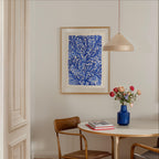 a dining area with a white table, a blue vase with flowers, and a framed print of blue and white floral designs hanging on the wall above the table.