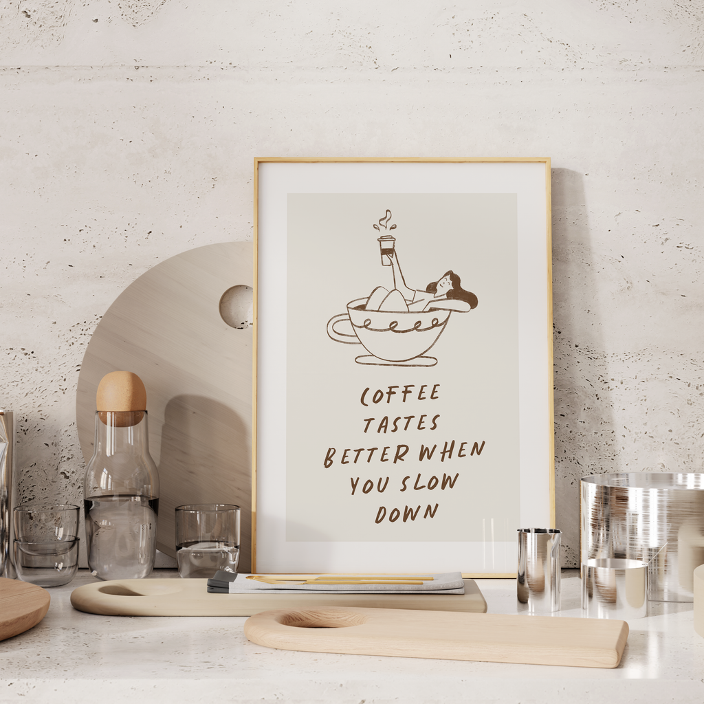 a framed poster with a cartoon illustration of a person relaxing in a cup of coffee, accompanied by the text "Coffee tastes better when you slow down".