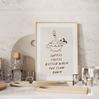 a framed poster with a cartoon illustration of a person relaxing in a cup of coffee, accompanied by the text "Coffee tastes better when you slow down".