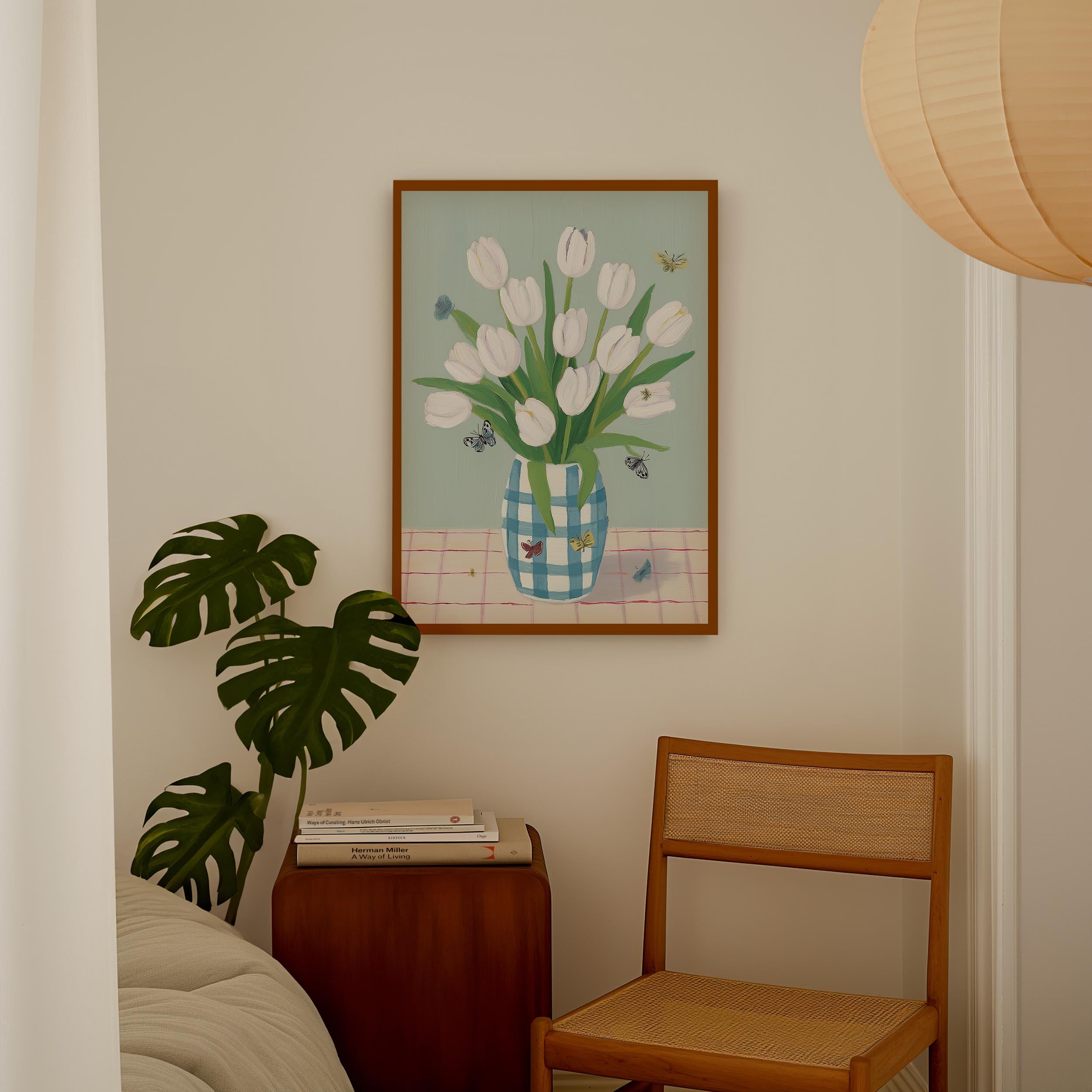 a cozy corner of a room with a framed painting of white tulips in a blue and white vase, a wooden chair, a stack of books, and a potted plant.
