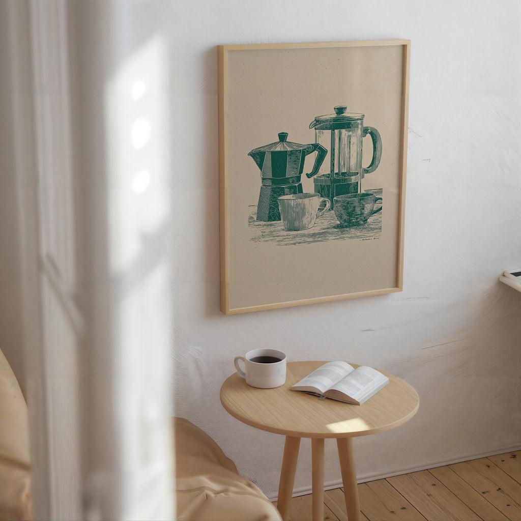 a cozy corner of a room with a wooden table, a white mug, and an open book, all set against a backdrop of a framed illustration of a coffee maker and a teapot.