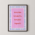 a framed poster with the text "sunrise, sunburn, sunset, repeat" written in a stylized font on a pink background.