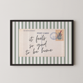 The image is a framed print with a postcard-style border and a handwritten message that reads "it feels so good to be home".