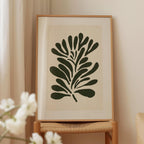 a framed artwork of a stylized plant or flower design, displayed on a wooden stand.
