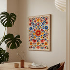 a vibrant, colorful floral print hanging on a wall above a wooden table with a vase of flowers and a plate of food.
