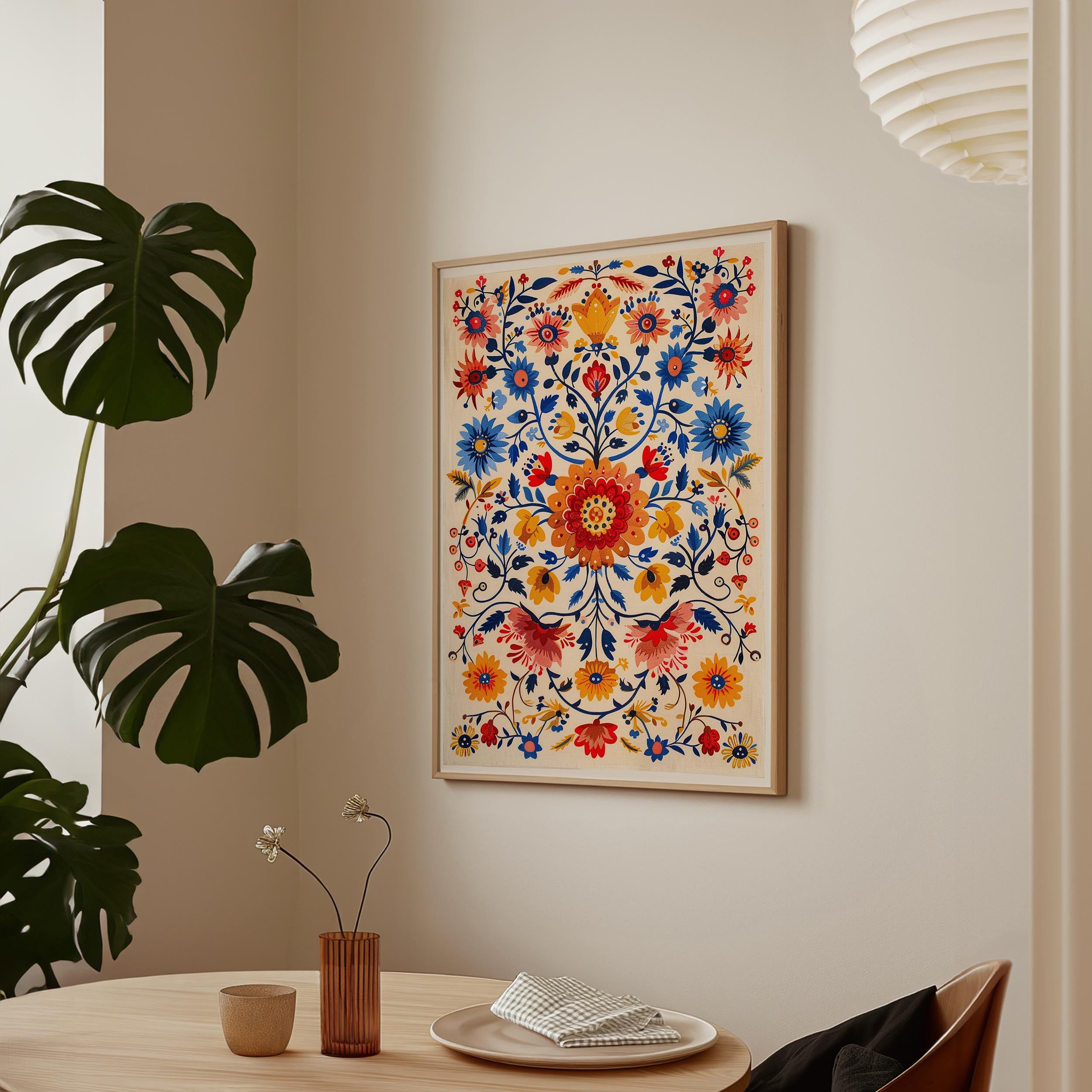 a vibrant, colorful floral print hanging on a wall above a wooden table with a vase of flowers and a plate of food.
