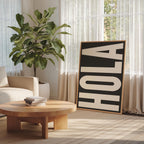 a living room with a large potted plant, a wooden coffee table, and a framed sign with the word "HOLA" on it.