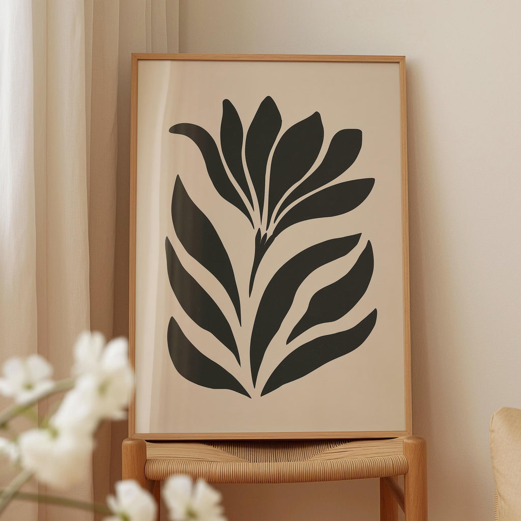 a framed artwork of a stylized flower or plant with black and white elements, displayed on a wooden chair against a light-colored wall.
