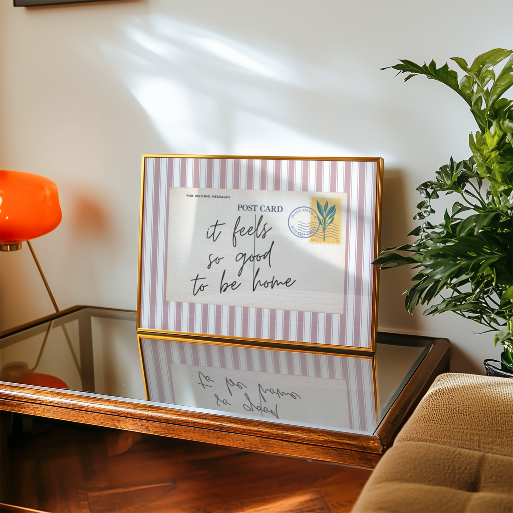 a framed postcard with a handwritten message, placed on a wooden table next to a potted plant.