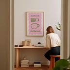 A woman is sitting at a wooden desk, surrounded by various objects, including a framed poster with the text "MATCHA MORNING" and illustrations of a cup and a bowl.