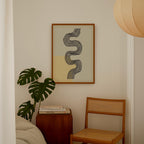 a cozy corner with a framed abstract artwork on the wall, a wooden chair, a small table with books, and a large monstera plant.