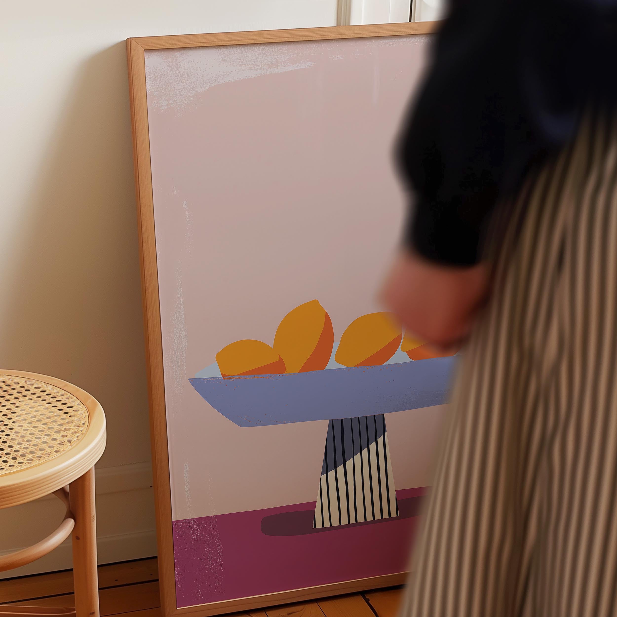 a person standing next to a framed artwork depicting a bowl of fruit on a table.