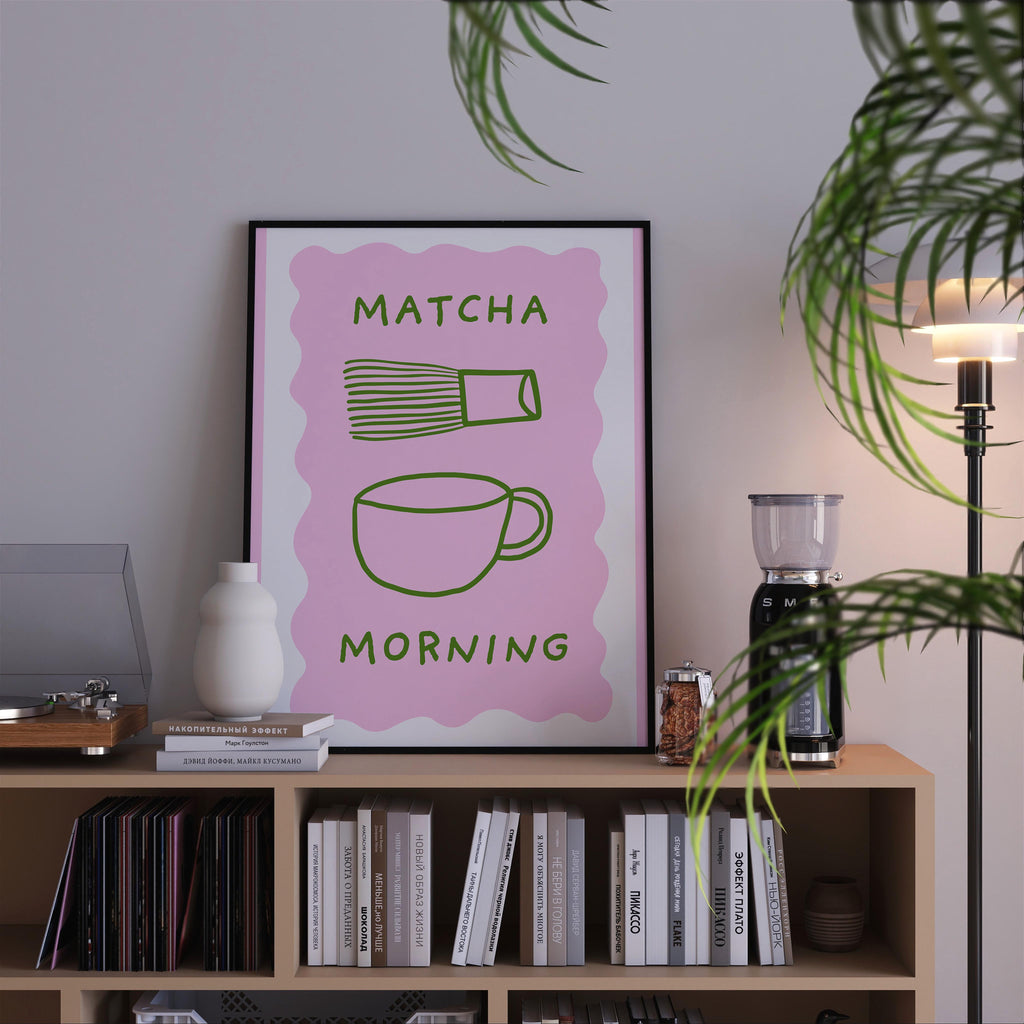 a pink poster with the text "MATCHA MORNING" displayed on it, placed on a bookshelf next to a lamp and other decorative items.