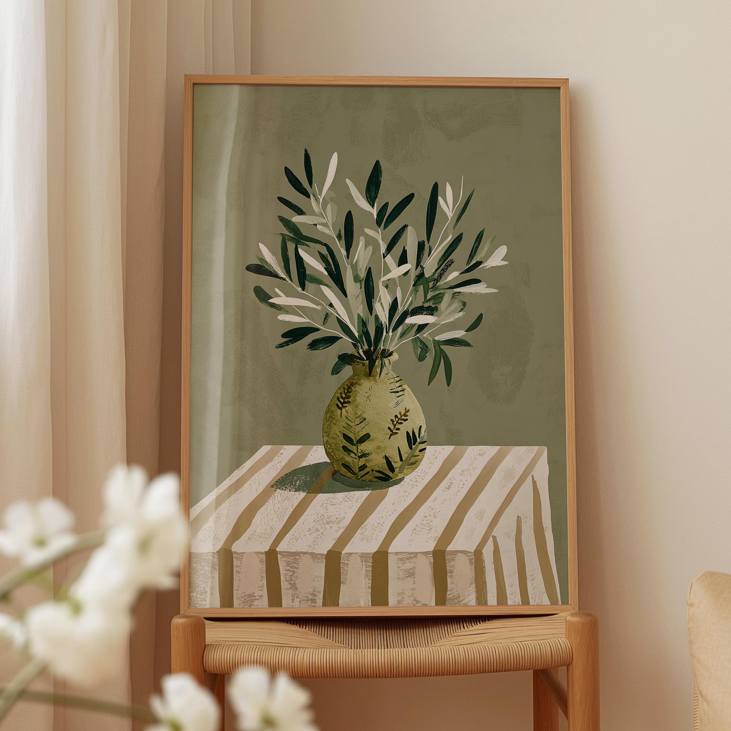 a framed painting of a vase with green leaves on a striped tablecloth.