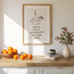 a framed poster with a cartoon illustration of a person drinking coffee, accompanied by the text "Coffee tastes better when you slow down". The poster is displayed on a wall above a wooden table with a bowl of oranges, a vase of flowers, and a stack of books.