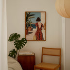 a cozy corner of a room with a painting of a woman in a red polka dot dress, a potted plant, a wooden side table, and a wooden chair.