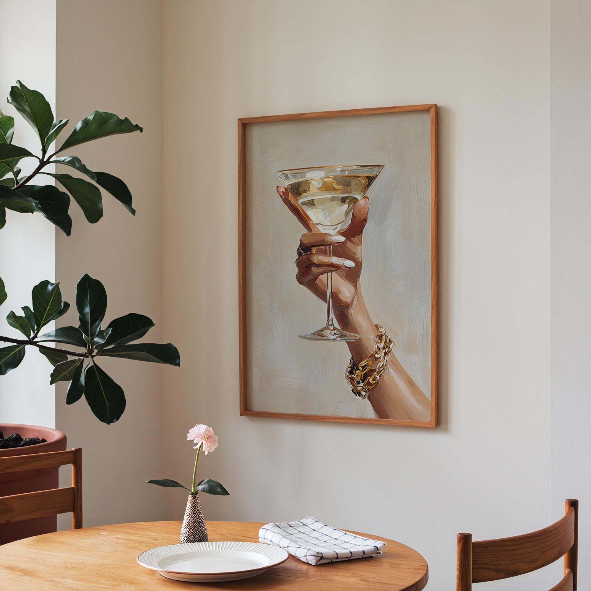 a framed painting of a hand holding a martini glass, with a vase of pink flowers and a plate of food on a wooden table in the foreground.