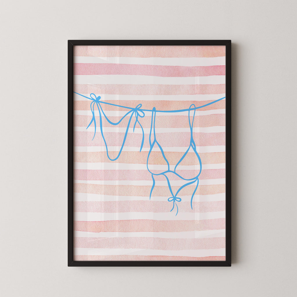 A framed print with a pink and white striped background and blue bra straps hanging from a line.