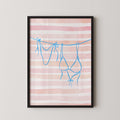 A framed print with a pink and white striped background and blue bra straps hanging from a line.