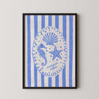 The image is a framed print featuring a blue and white design with a central illustration of a seahorse, starfish, and seashell, surrounded by blue and white striped patterns.