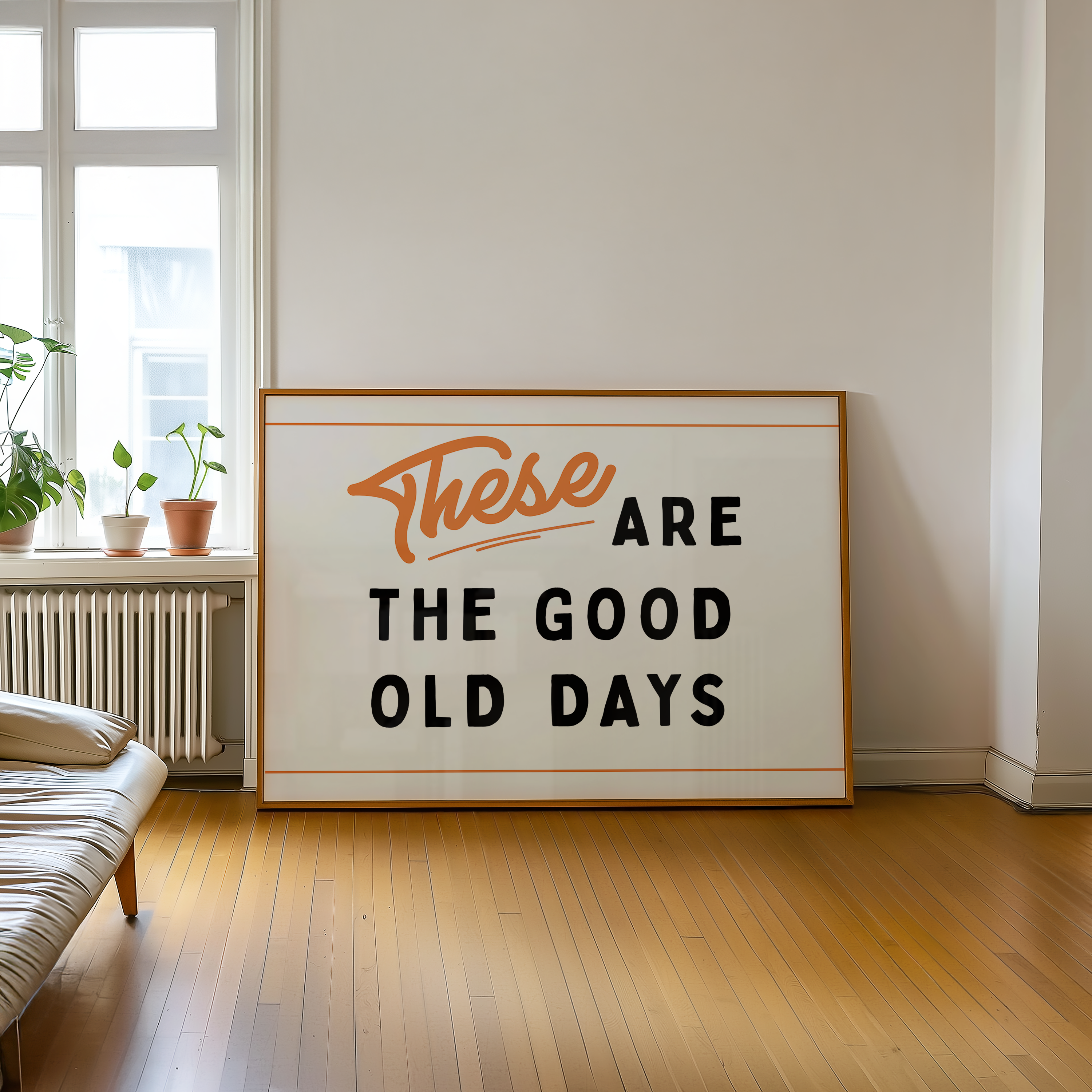 a large framed sign with the text "These are the good old days" on it, placed on a wooden floor in a room with a window and a plant.