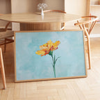 a large framed painting of a yellow flower on a wooden table.